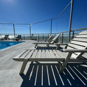 Tybee sand chaise lounge chairs on a deck with a pool and ocean view under a clear blue sky.